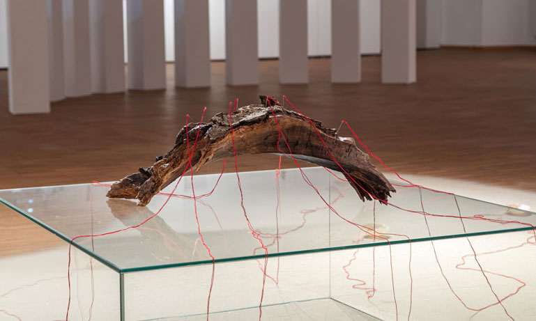 ANJA ASCHE – Entfaltung. 
Installation – Holzstück, Wachs, Fäden, Nadeln, Sand, Podest, ca. 400 x 350 cm, 2023